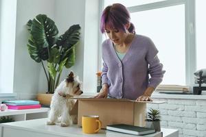 Excited young woman opening box while her cute dog sitting near her on the table photo