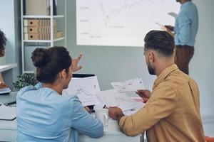 Group of young modern people in smart casual wear analyzing data on projection screen in the office photo