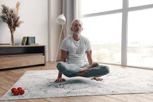 Active senior man in sport clothing meditating while standing on hands in the yoga position at home photo