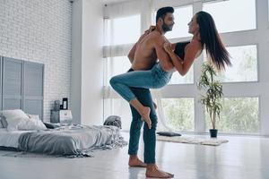 Couple enjoying dancing. Full length of beautiful young couple embracing and smiling while dancing in the bedroom photo