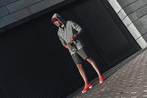 After workout. Full length of young man in sports clothing relaxing and looking away while standing outside photo