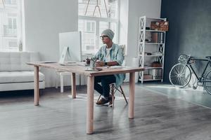 poner ideas en algo real. un joven apuesto con anteojos mirando el monitor mientras se sienta en su lugar de trabajo en una oficina creativa foto