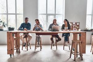 compartiendo ideas. grupo de jóvenes modernos con ropa informal elegante discutiendo negocios mientras trabajan en la oficina creativa foto