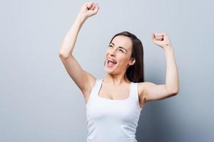 Can not hide her emotions. Beautiful young women keeping arms raised and smiling while standing against grey background photo