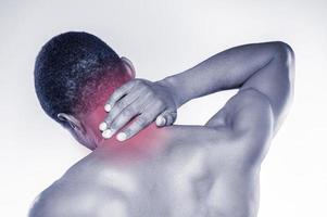 sintiendo dolor en el cuello. vista trasera de un joven africano musculoso tocándose el cuello mientras se enfrenta a un fondo gris foto