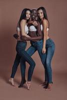 Looking gorgeous Full length of three attractive young women looking at camera and smiling while standing against brown background photo