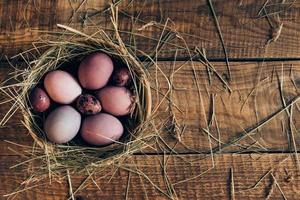 Ester nest. Top view of colored Easter eggs in bowl with hay lying on wooden rustic table photo