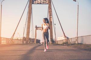 Just keeping running. Full length of beautiful young woman in sports clothing running along the bridge photo