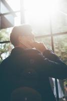 Talking about business. Low angle rear view of confident young man talking on the mobile phone and looking away while standing in front of the big window indoors photo