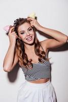 Playful beauty. Cheerful young woman holding cupcakes over her head while standing against white background photo