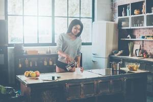 Morning coffee. Beautiful young African woman pouring coffee to cup and smiling while standing in kitchen at home photo