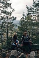 tiempo de descansar. hermosa pareja joven sentada en las rocas y sonriendo mientras caminan juntos en el bosque foto