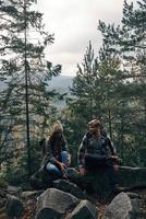 Time to rest. Beautiful young couple sitting on the rocks and smiling while hiking together in the woods photo