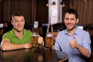 amigos bebiendo cerveza. dos jóvenes sosteniendo tazas con cerveza y sonriendo a la cámara foto