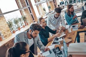 Group of young modern people in smart casual wear communicating and using modern technologies while working in the office photo