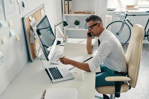 Good to hear from you Top view of good looking young man talking on the phone while sitting in the office photo