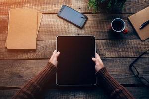 Technologies make life easier. Close-up top view image of woman holding digital tablet with copy space while sitting at the rough wooden table photo