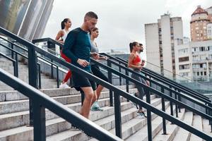 Group of young people in sports clothing jogging while exercising on the stairs outdoors photo