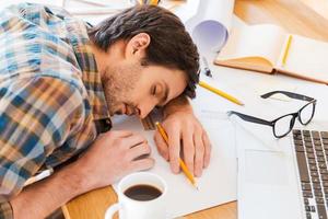 Feeling exhausted. Top view of young man sleeping while sitting at his working place photo