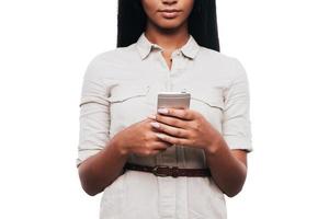 Typing quick message. Cropped image of confident young African woman holding mobile phone while standing against white background photo