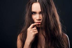 Piercing glance. Confident young shirtless woman holding finger on her lips and looking at camera while standing against black background photo