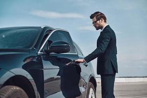 propietario del coche de estado. apuesto joven hombre de negocios entrando en su coche mientras está de pie al aire libre foto