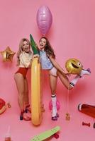 Enjoying carefree time. Full length of two attractive young women in swimwear smiling and looking at camera while standing against pink background photo