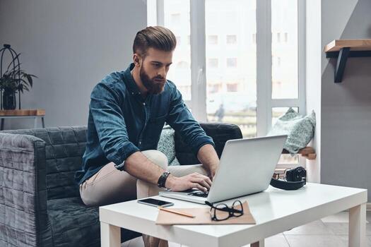 Concentraiting on project. Thoughtful young modern man using computer while sitting at his working place photo