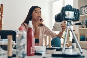 Fashionable young woman applying lipstick while making social media video photo