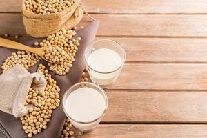 Soy milk in a glass with soybeans on a wooden table organic drink high protein healthy breakfast agricultural produce vegetarian - top view photo