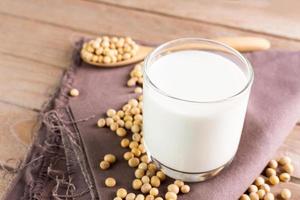 Soy milk in a glass with soybeans on a wooden table organic drink high protein healthy breakfast agricultural produce vegetarian - top view photo