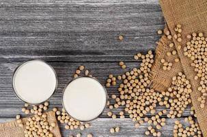 Soy milk in a glass with soybeans on a wooden table organic drink high protein healthy breakfast agricultural produce vegetarian - top view photo