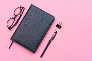 Black glasses, notebook and pen. Subjects for training and business on a pink photo