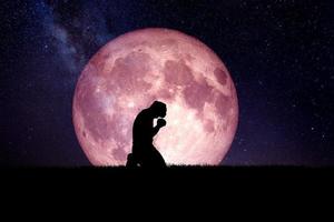 A desperate and lonely man knelt down and prayed to God. There is a moon in the background at night. Desperate, heartbreaking, and lonely concepts photo