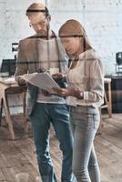 Working together. Two business colleagues working with documents while standing behind the glass wall in the board room photo