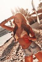 Naturally fit and beautiful. Attractive young woman smiling and holding a cocktail while standing on the beach near the bar counter photo