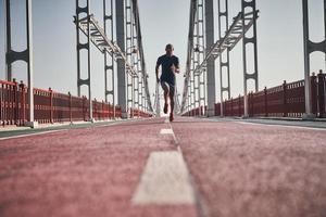 Always in great shape. Full length of young African man in sports clothing exercising while jogging on the bridge outdoors photo