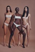 Pure perfection. Full length of three attractive mixed race women looking at camera while standing against brown background photo