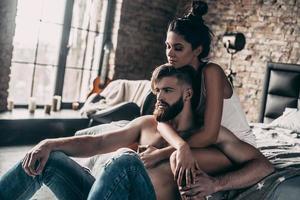 día perezoso en casa. apuesto joven hipster con barba sentado en el suelo mientras una hermosa chica lo rodea con los brazos foto