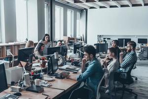 ajetreado día de trabajo. grupo de jóvenes empresarios que se concentran en su trabajo mientras se sientan juntos en el gran escritorio de la oficina foto