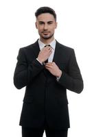 Used to look perfect. Handsome young man in full suit adjusting his necktie and looking at camera while standing against white background photo