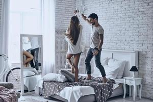Going crazy together. Full length of playful young couple dancing on the bed and smiling photo