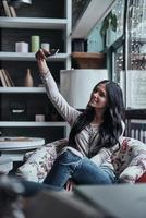 segura de su estilo. Atractiva joven mujer sonriente tomando selfie usando su teléfono inteligente mientras está sentada en el restaurante foto