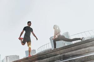 preparación de los músculos para las acciones. toda la longitud de una pareja joven con ropa deportiva haciendo ejercicios de estiramiento juntos foto