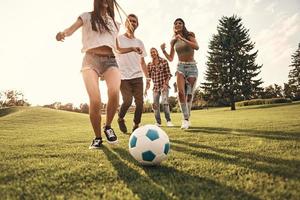Group of young smiling people in casual wear running while playing soccer outdoors photo