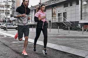 Never stop. Full length of young couple in sport clothing running through the city street together photo