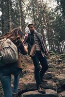 Giving a hand of help. Young couple holding hands and moving up while hiking together in the woods photo