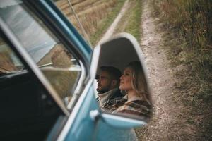 pareja feliz viajando. reflejo de una hermosa pareja joven mirando hacia otro lado y sonriendo mientras se sienta en una mini furgoneta de estilo retro foto