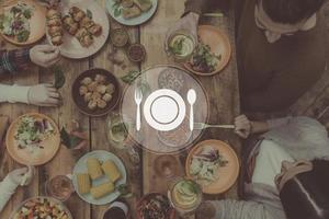 reunirse para la cena. imagen compuesta digitalmente de utensilios de cocina sobre la vista superior de cuatro personas cenando juntas mientras se sientan en la mesa rústica de madera foto