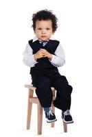 Little gentleman. Little African baby boy looking at camera while sitting on stool against white background photo